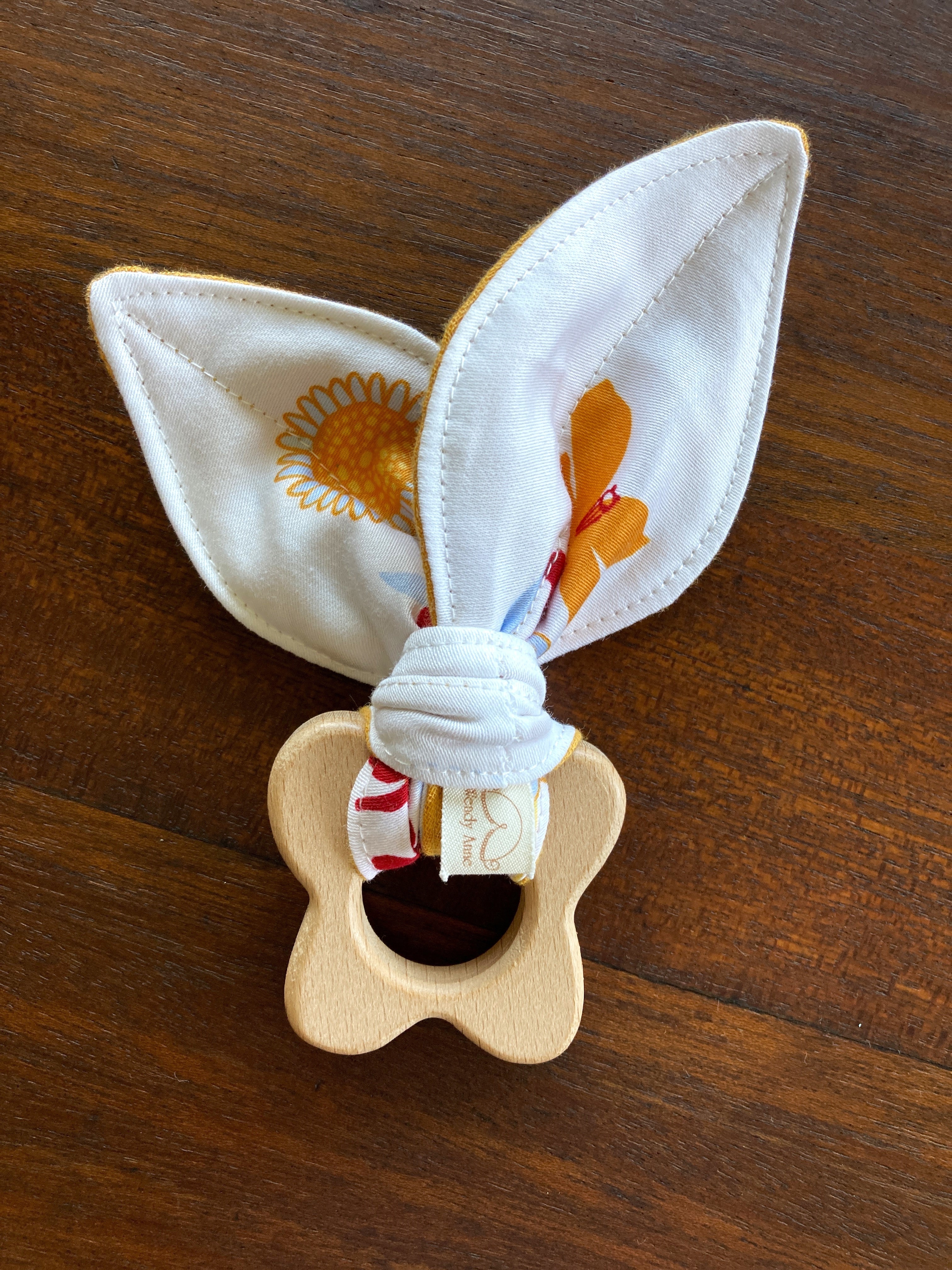 Wooden teething ring with bunny ears and a colorful band on a wooden surface