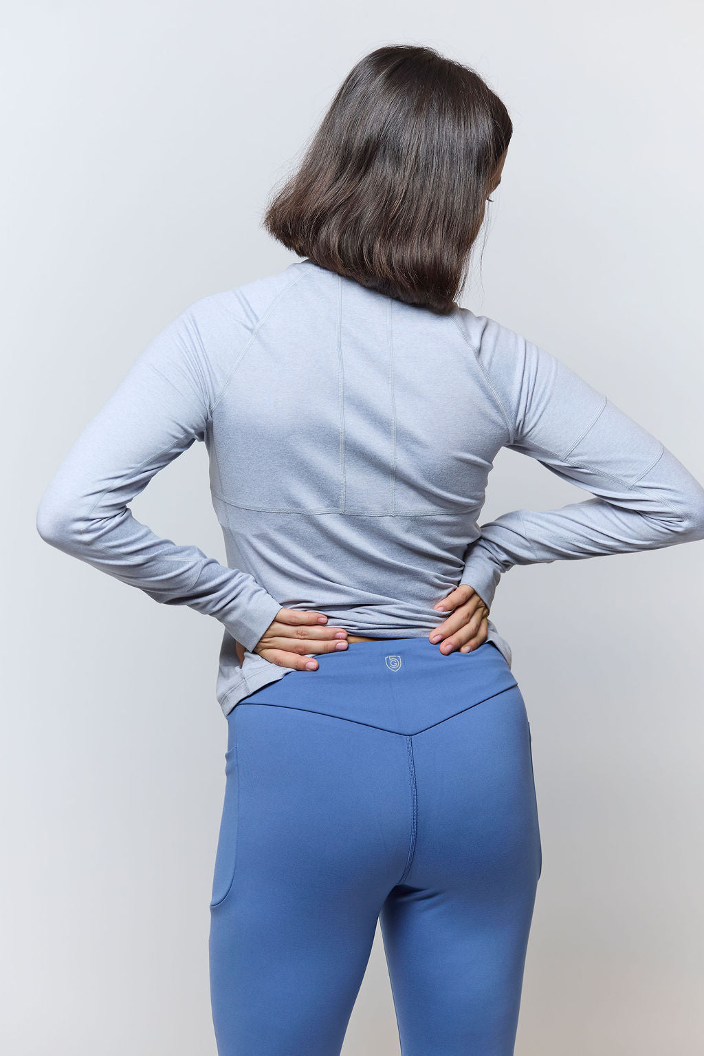 Person wearing a light gray long-sleeve top and blue leggings against a white background