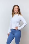 Woman wearing a white long-sleeve top and blue leggings against a plain background