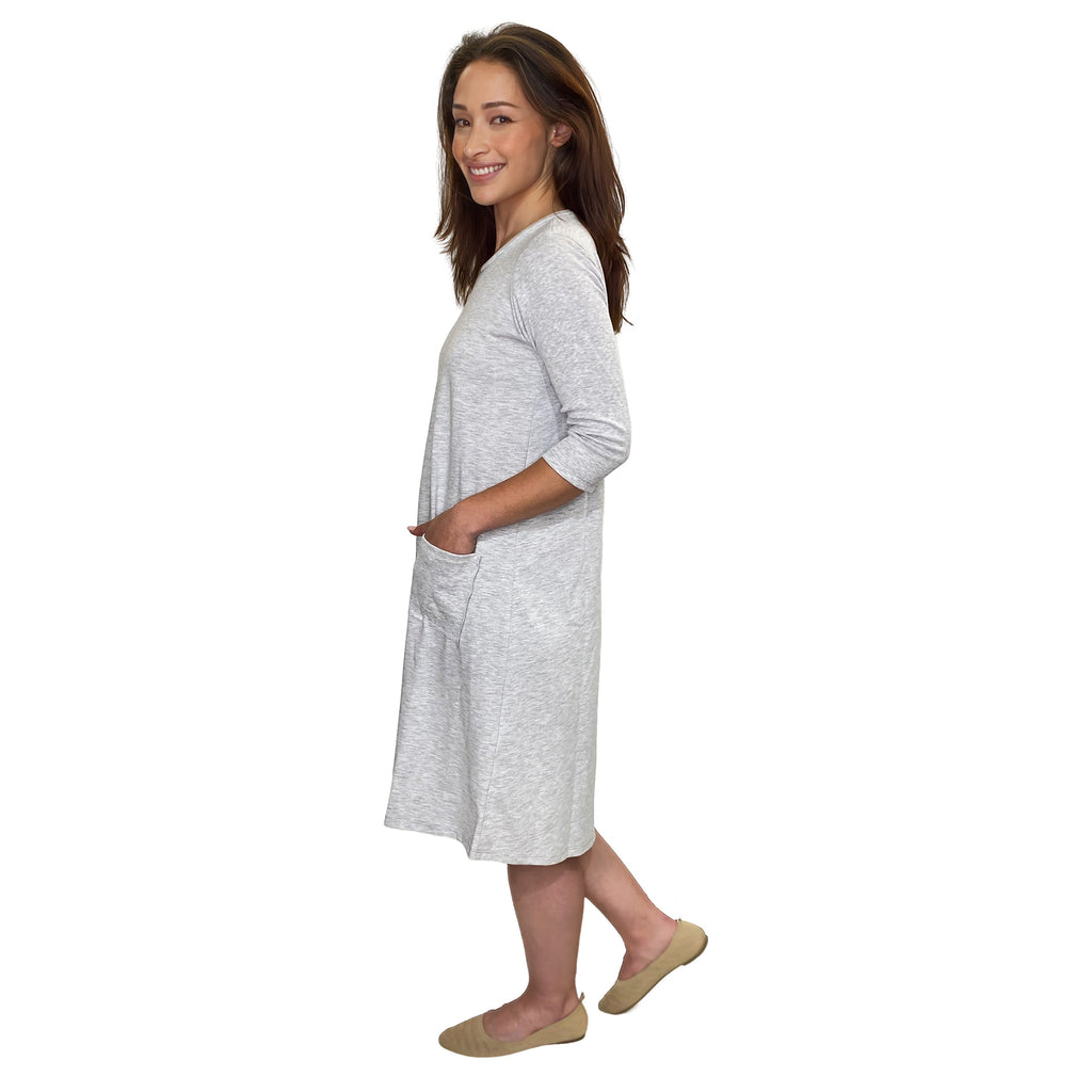 A woman modeling a light gray heathered three-quarter sleeve tunic dress with side pockets, shown from a side profile against a plain white background.