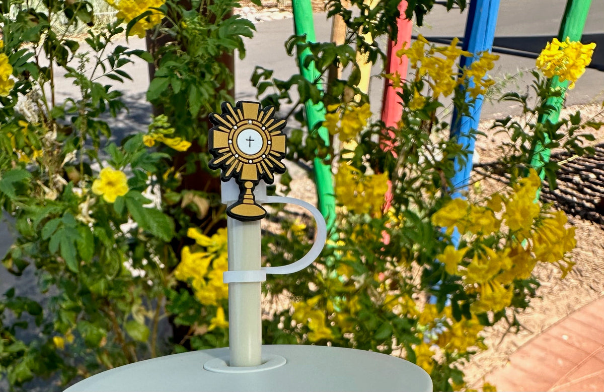 Decorative item with a cross on top of a white container against a background of yellow flowers and colorful poles.