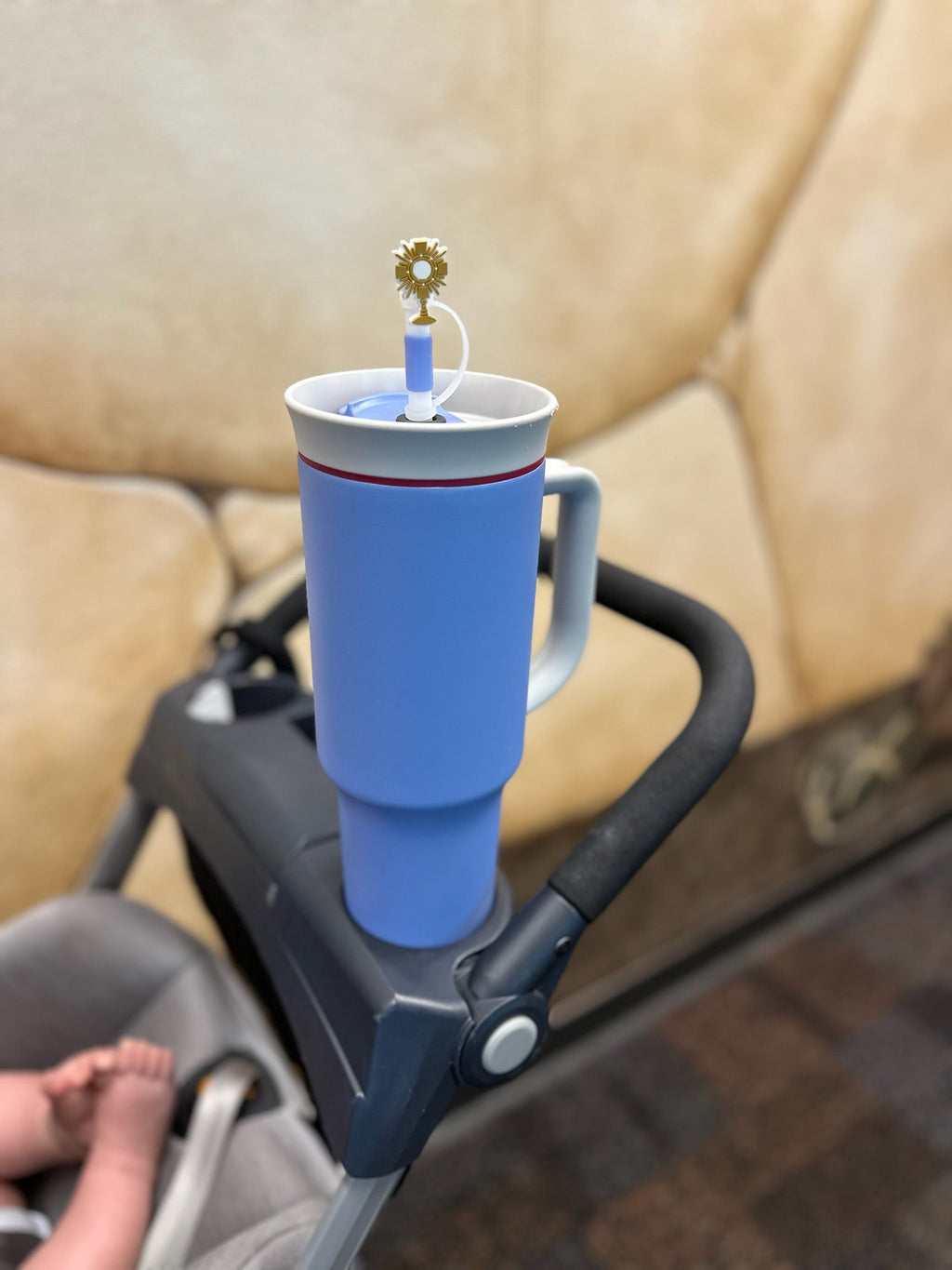 Blue cup holder attached to a stroller with a blue cup inside, on a beige couch background.