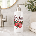 Soap dispenser with 'Shalom Sweet Home' text and pomegranate design on a bathroom counter.