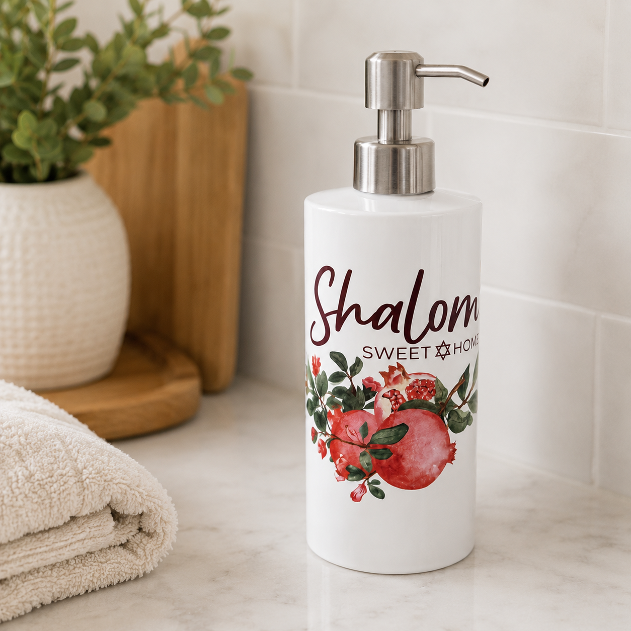 White soap dispenser with 'Shalom Sweet Home' text and pomegranate design on a bathroom counter.