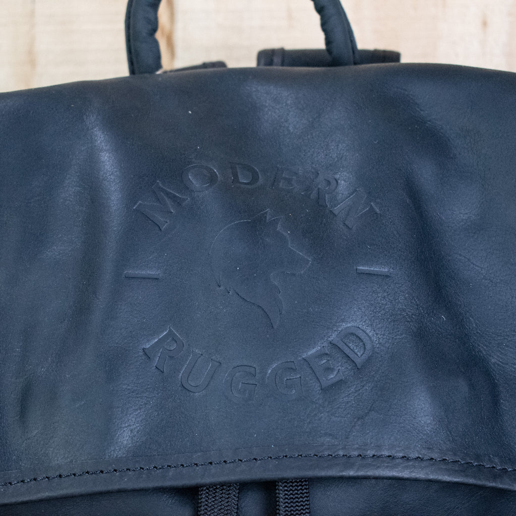 Black leather bag with 'Modern Rugged' embossed text on a beige background