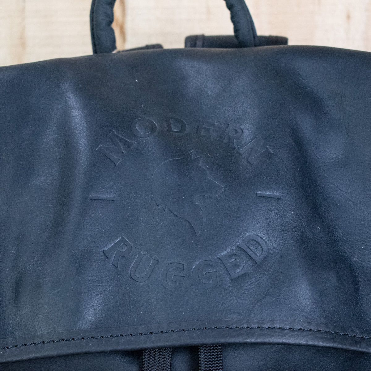 Black leather bag with 'Modern Rugged' embossed text on a beige background