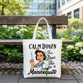 Tote bag with a nurse graphic and text 'Calm Down I've Done This on a Mannequin' on a bench outdoors.