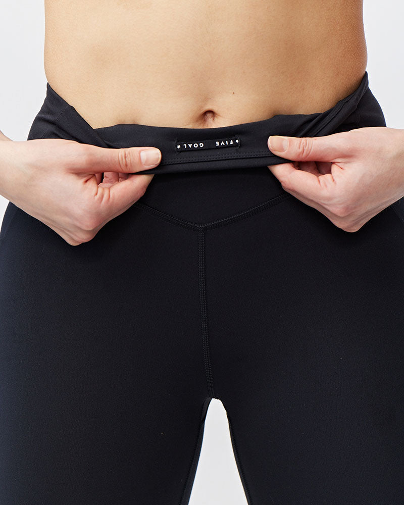 Person wearing black leggings with a visible brand logo on a plain background