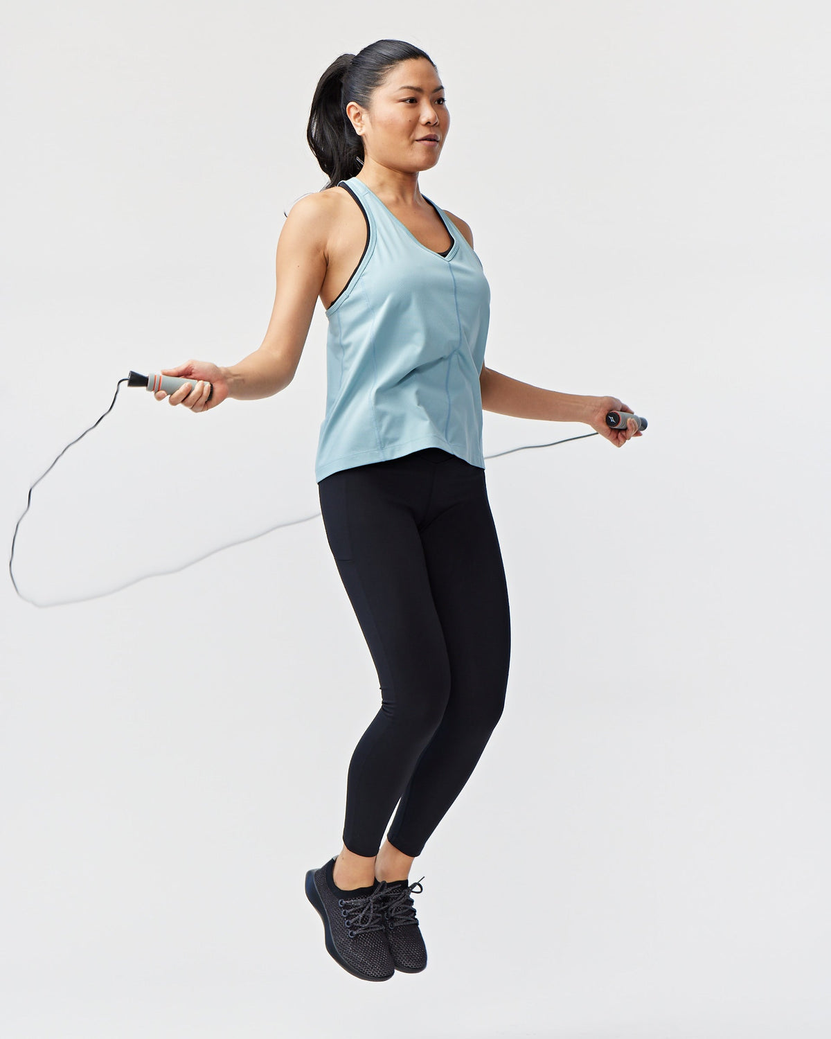 Woman jumping rope on a light gray background