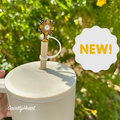 White tumbler with a religious-themed straw topper labeled 'NEW!' against a green outdoor background.