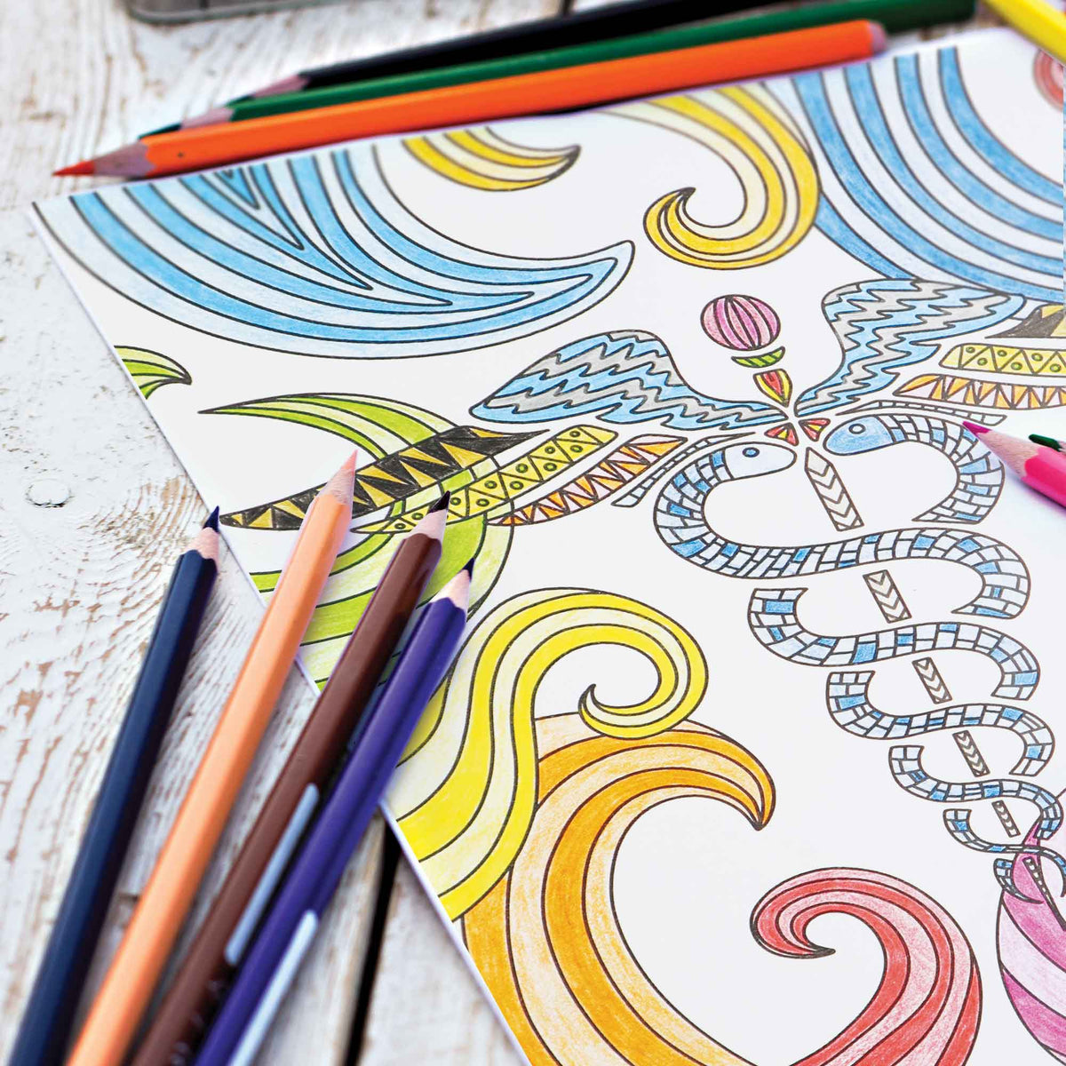 Coloring book with abstract designs and colored pencils on a wooden surface