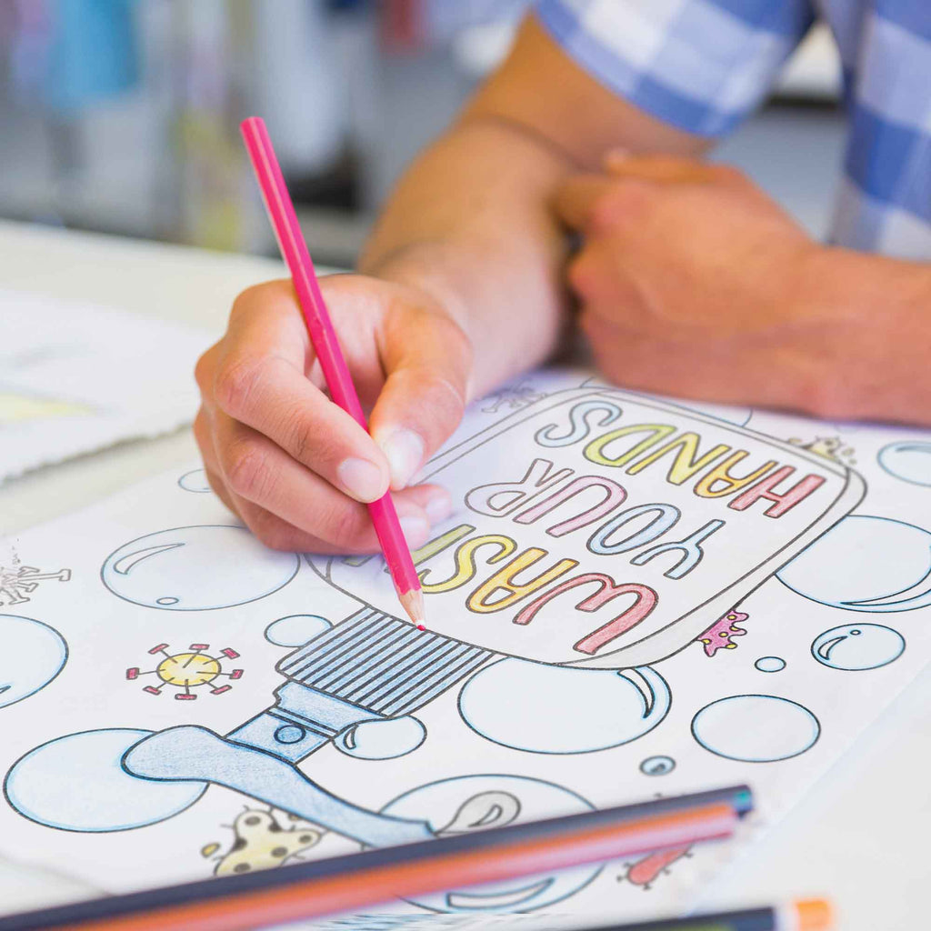 Person coloring a book with a pink crayon, surrounded by educational materials.