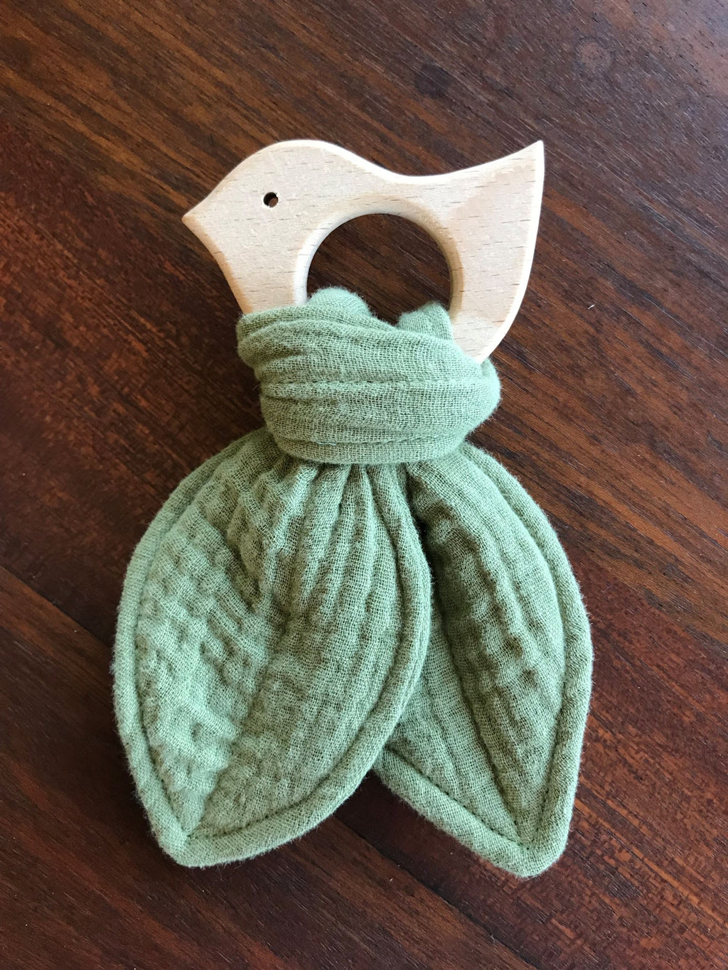 Green textured teething ring with wooden base on a wooden surface