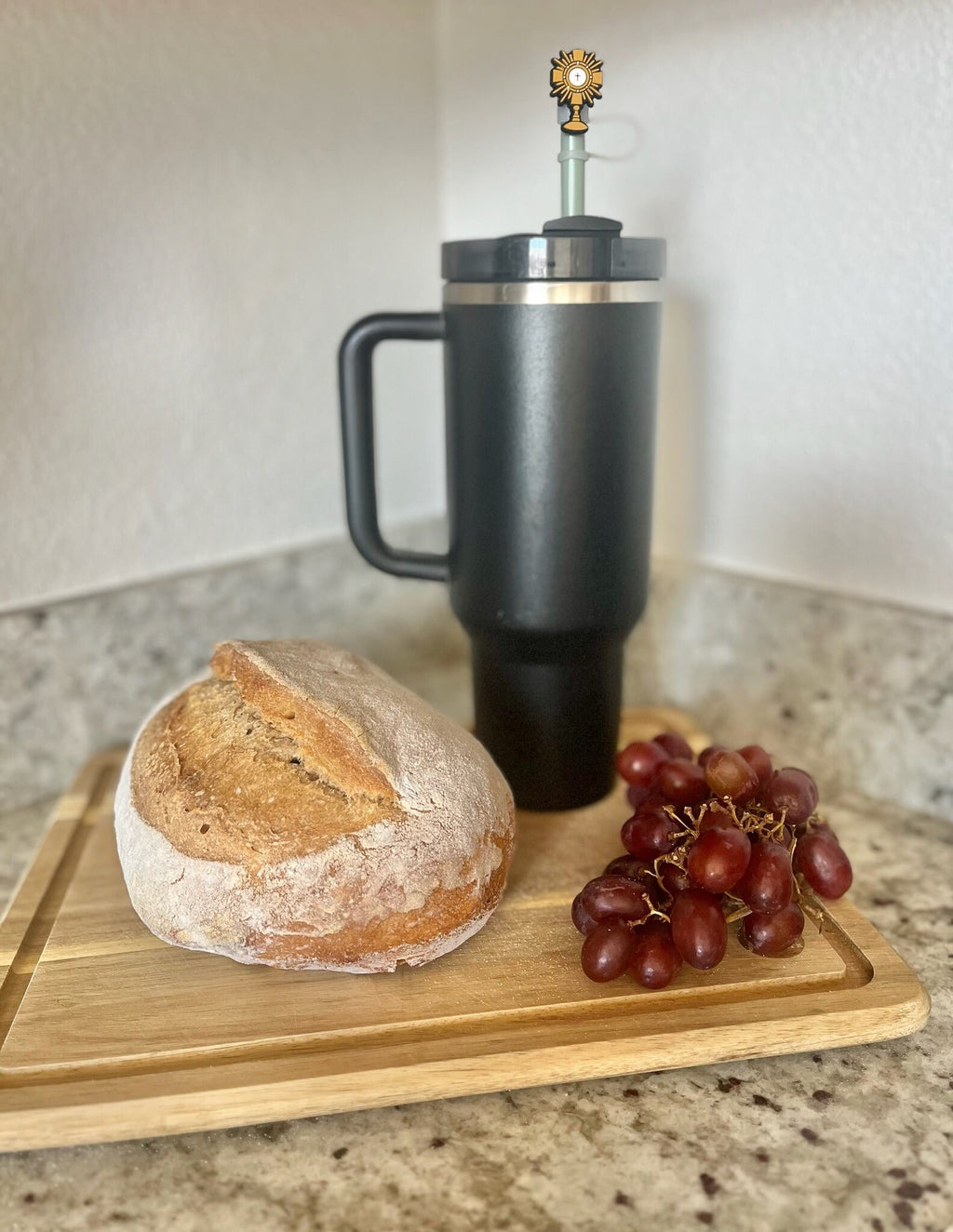Black insulated mug on a wooden cutting board with bread and grapes