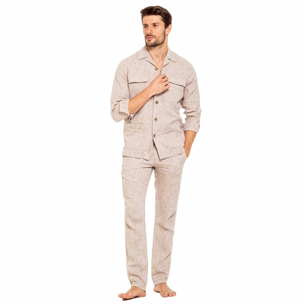 A man modeling a light beige linen pajama set consisting of a long-sleeve button-up shirt and matching pants, standing against a solid white background.