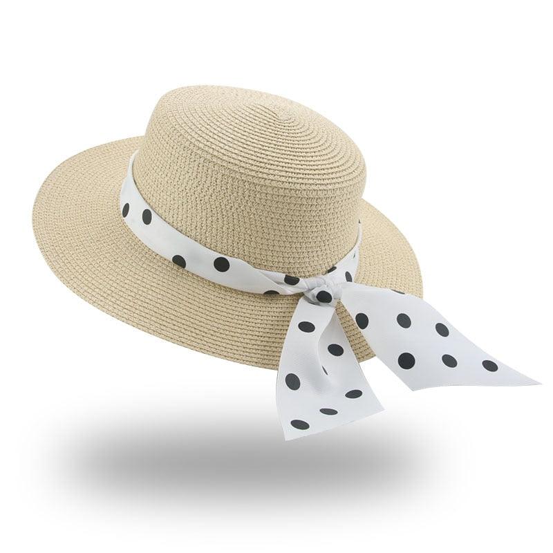 Beige straw hat with a white ribbon featuring black polka dots on a white background