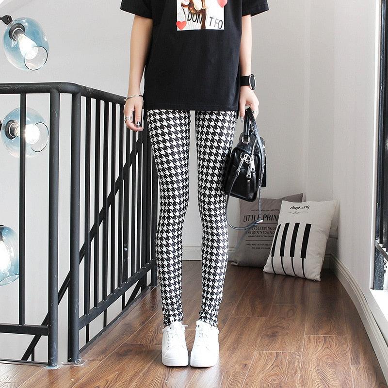 Person wearing a black t-shirt, houndstooth patterned pants, and white sneakers in an indoor setting.