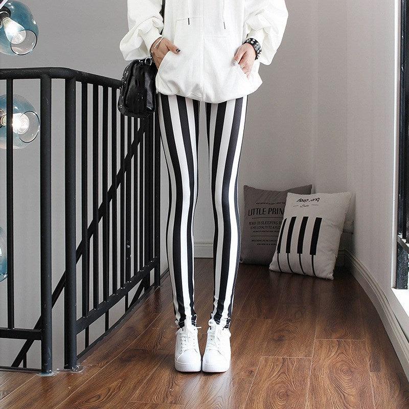 Person wearing a white jacket and black and white striped pants in a room with a black railing and pillows.