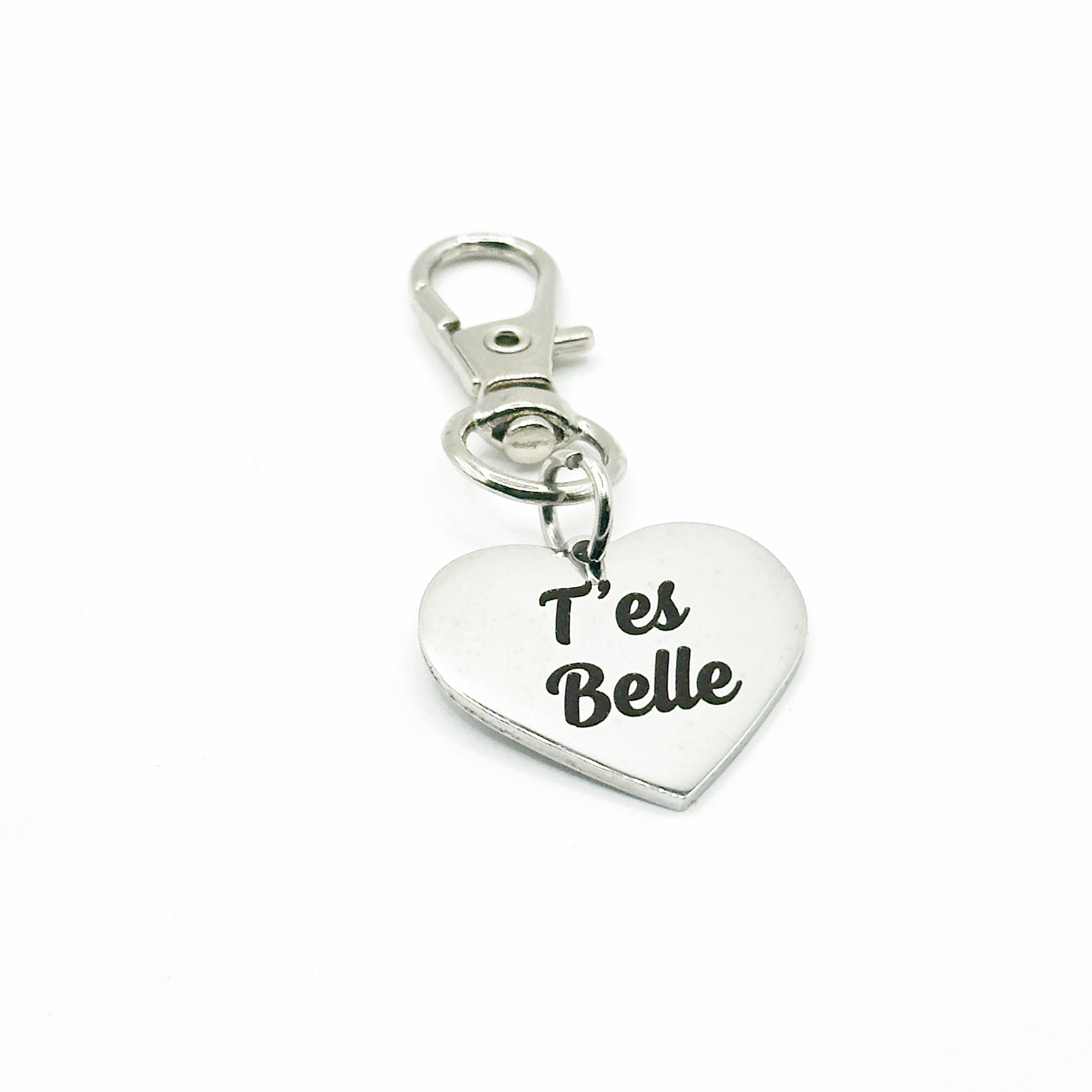 A silver-toned metal heart-shaped charm keychain with the phrase 'T'es Belle' printed in black script, attached to a matching lobster clasp on a plain white background.