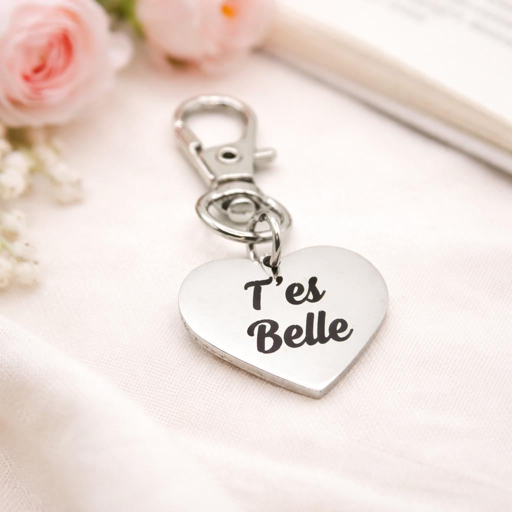 Heart-shaped keychain with 'T'es Belle' text on a light background with flowers.