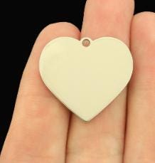 Heart-shaped silver pendant held in a hand against a black background