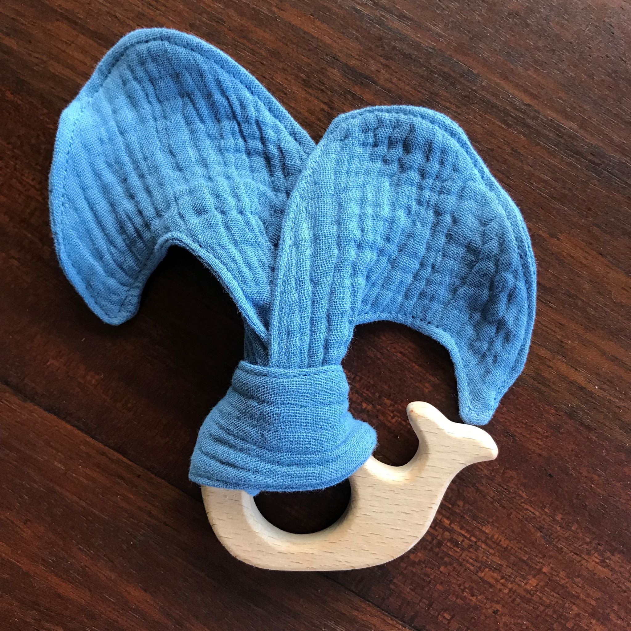 Blue textured teething ring with a wooden whale design on a wooden surface
