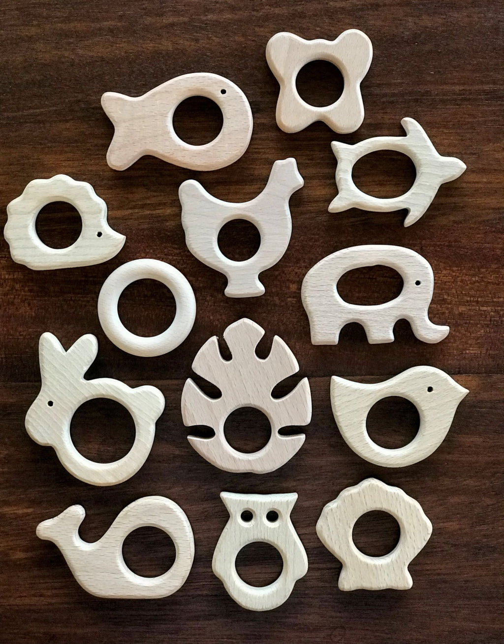 Set of white animal-shaped wooden teethers on a dark wooden surface